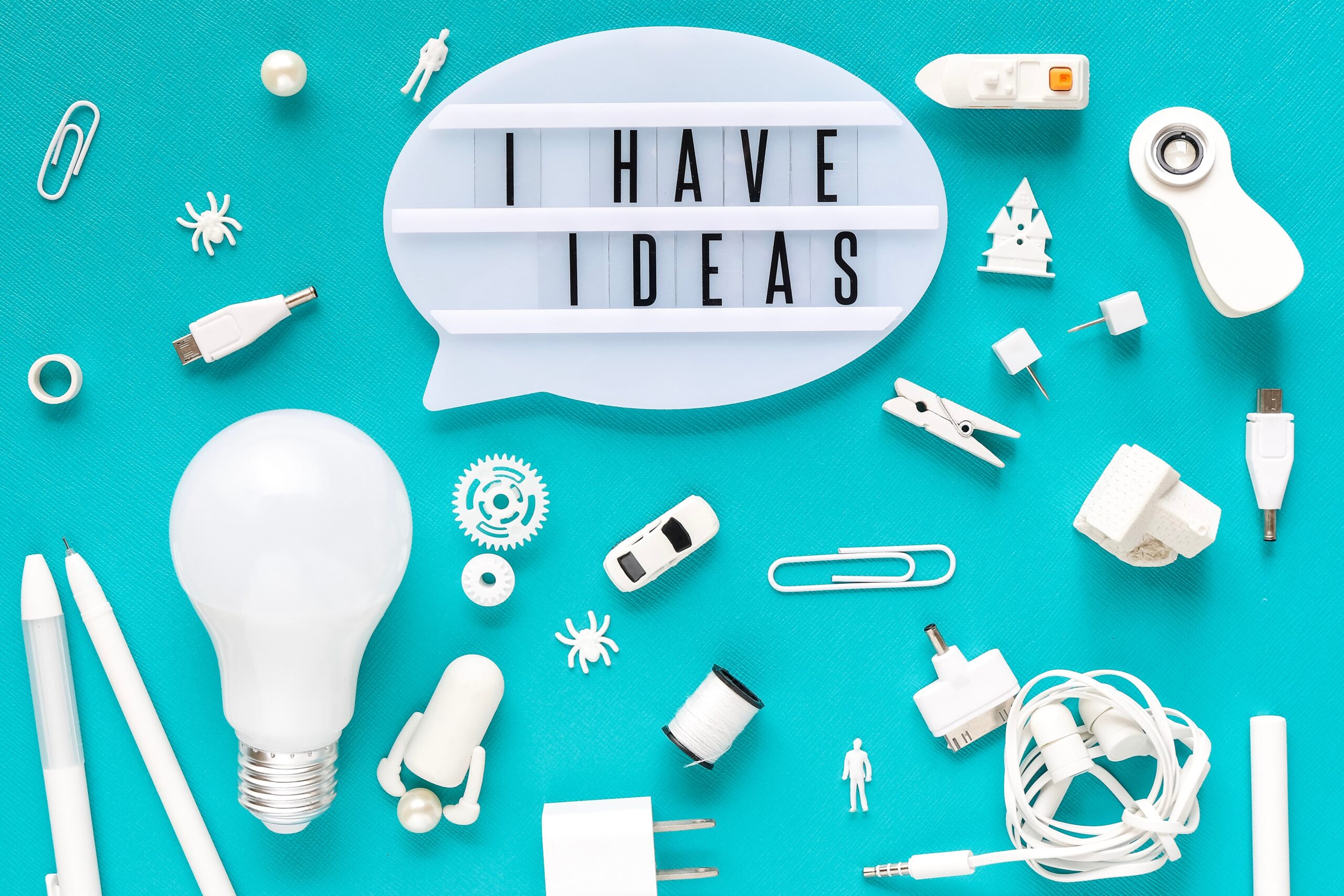 Objetos creativos sobre fondo turquesa con cartel que dice “I HAVE IDEAS”, representando la generación de ideas de emprendimiento e innovación