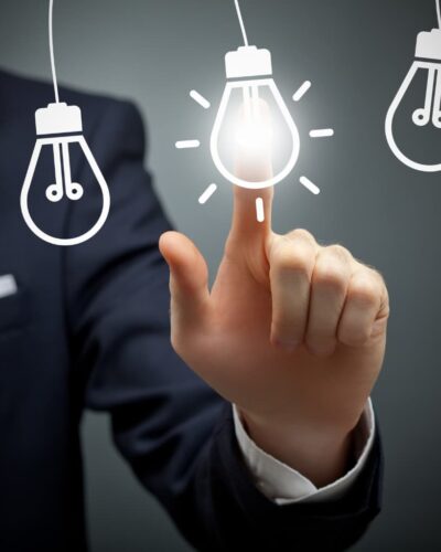 Hombre de negocios tocando una bombilla encendida entre varias apagadas, representando la elección de una idea de emprendimiento innovadora