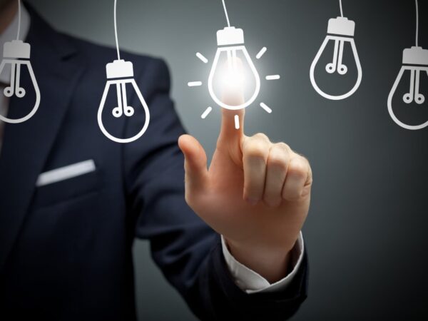 Hombre de negocios tocando una bombilla encendida entre varias apagadas, representando la elección de una idea de emprendimiento innovadora