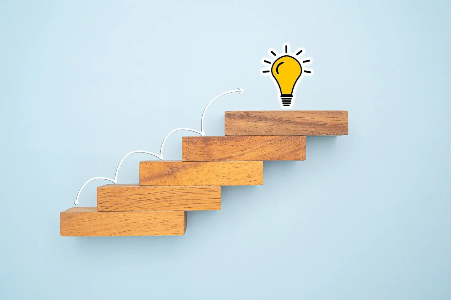 Escalones de madera en forma ascendente con una bombilla encendida en la parte superior, simbolizando el progreso o el camino hacia una idea o logro.